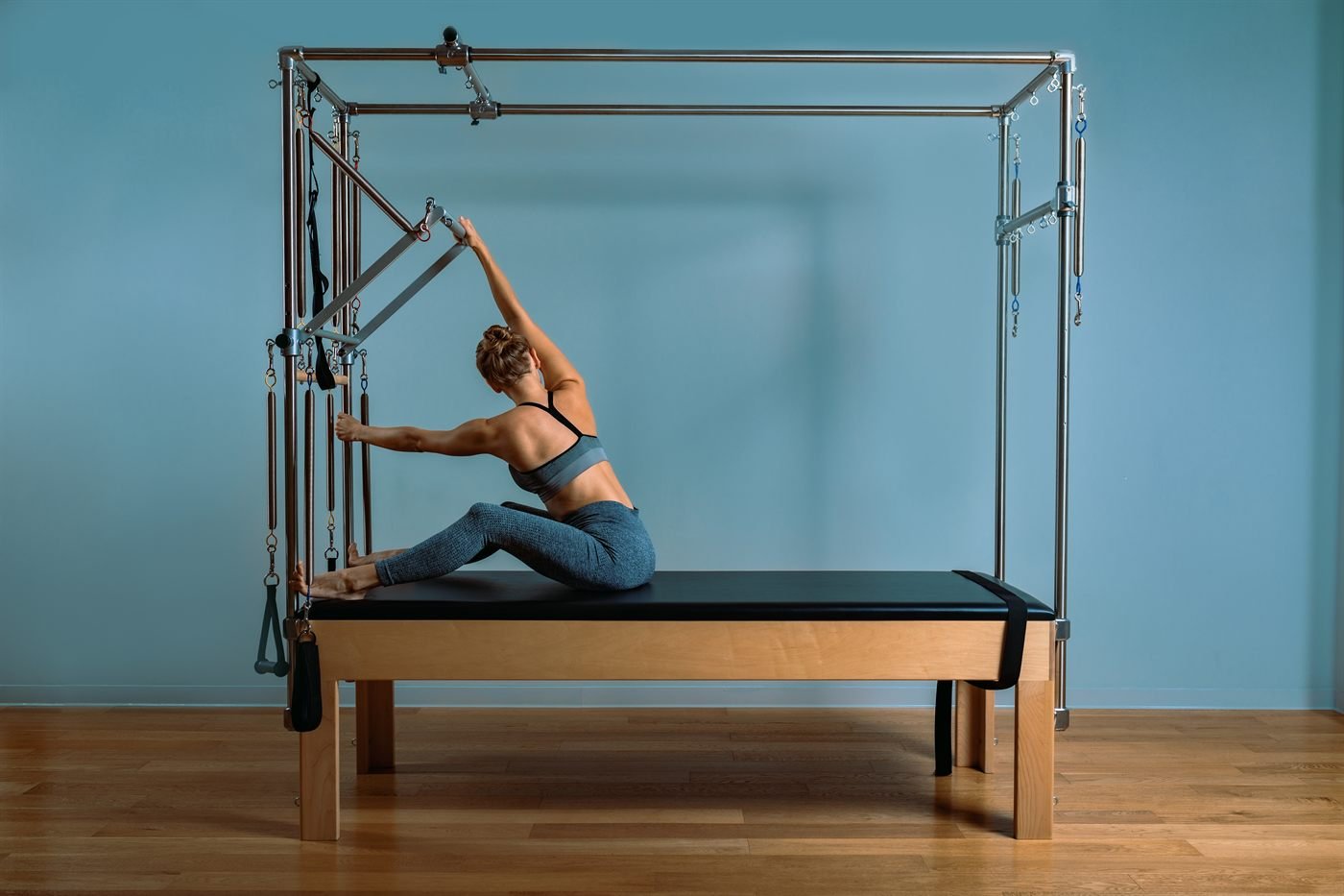 Mulher alongando a coluna sentada no cadillac, aparelho de Pilates com estrutura de madeira e molas