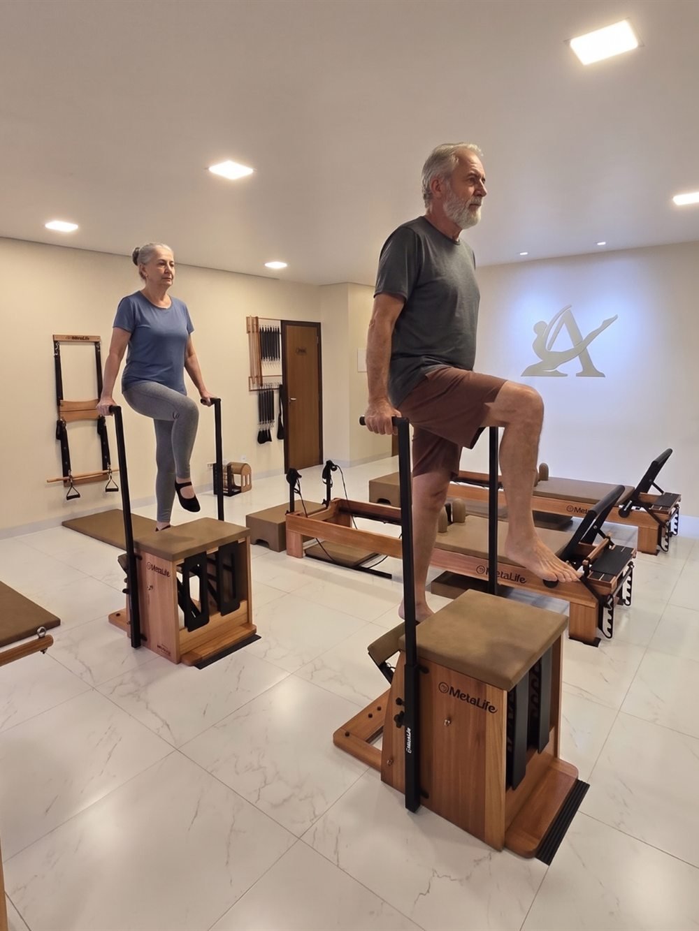 Casal de alunos na melhor idade em exercício de equilíbrio sobre as chairs, no salão do estúdio Aura